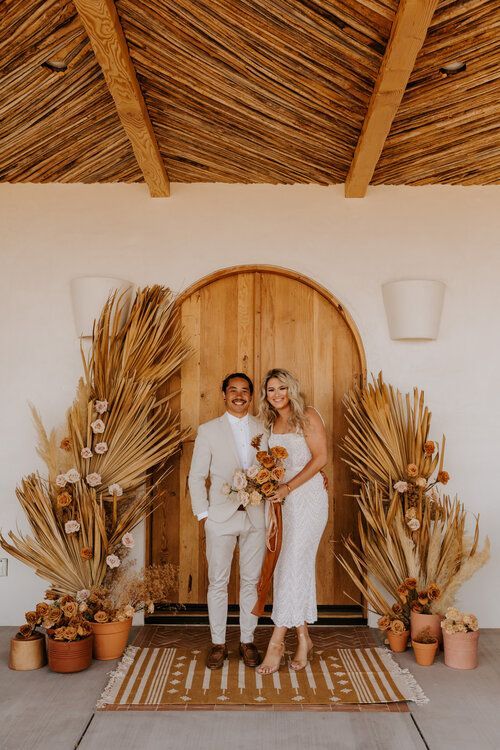 a very simple boho fall wedding backdrop of wooden doors, dried fronds and blush blooms on each side is a lovely idea for a fall boho wedding