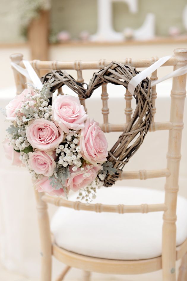 a vine heart shaped wreath with baby's breath, pink roses and pale leaves is a cool rustic chair decoration