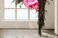 a wedding ceremony space with a bold rug, greenery and red blooms and a bold neon heart sign hanging is cool