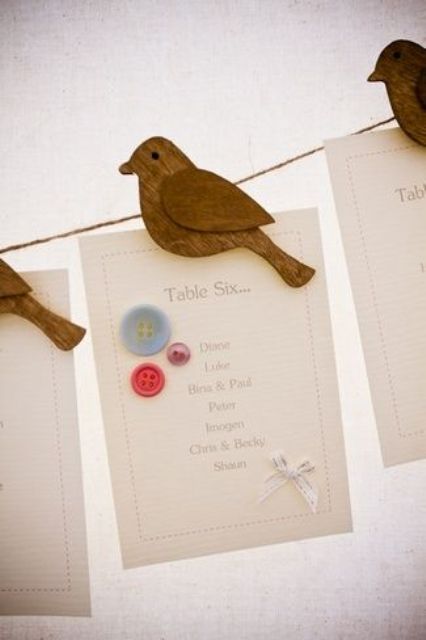 a wedding seating chart done with cards with tables and wooden birds hinting on love birds is a cool rustic wedding idea