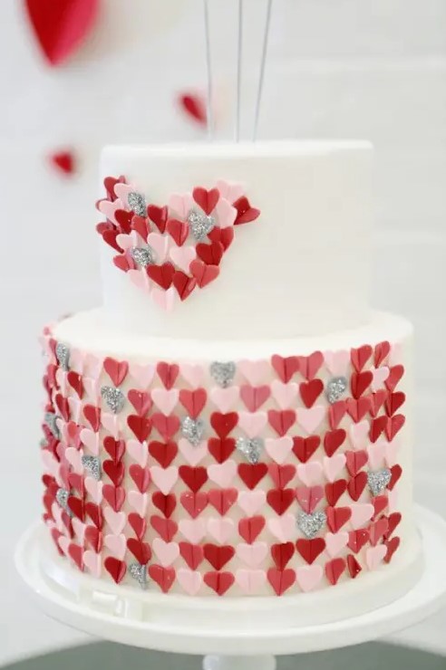 a white wedding cake decorated with pink, grey and red hearts   they cover the lower tier and form a heart on the upper one