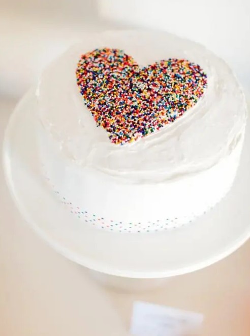 a white wedding cake with a colorful conetti heart on top is a lovely and beautiful idea for a Valentine wedding