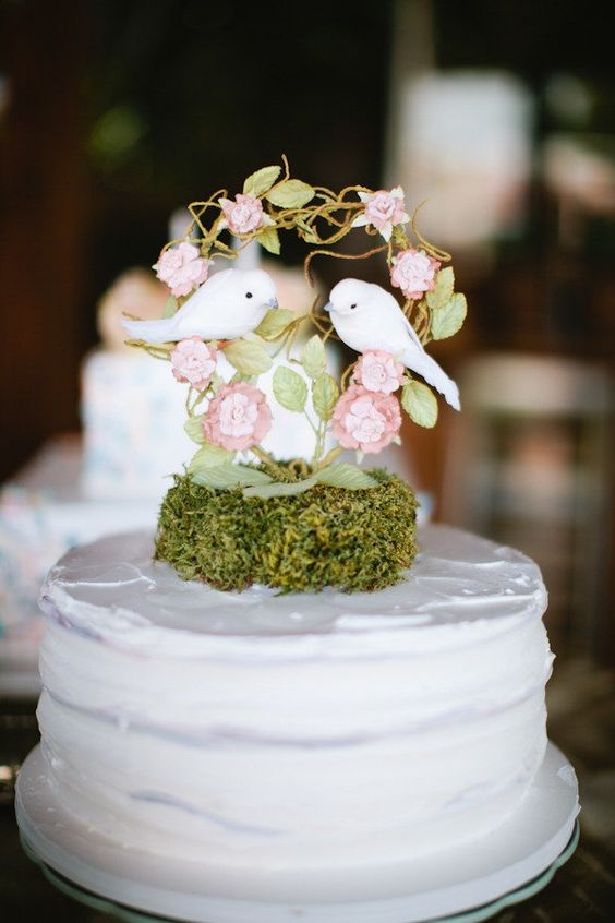a white wedding cake with moss, a mini cake topper with a tree with two love birds is a cute idea for a wedding