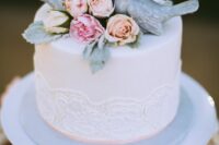 a white wedding cake with patterns, blush and pink blooms on top and some pale leaves, blue porcelain bird cake toppers