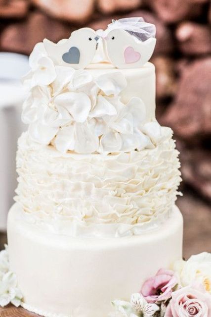 a white wedding cake with ruffle and sleek tiers, with love bird cake toppers is a cool idea for a wedding