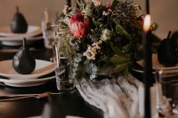 an elegant moody tablescape with a textural and herb centerpiece, black candles and pears and a black table is chic for Halloween