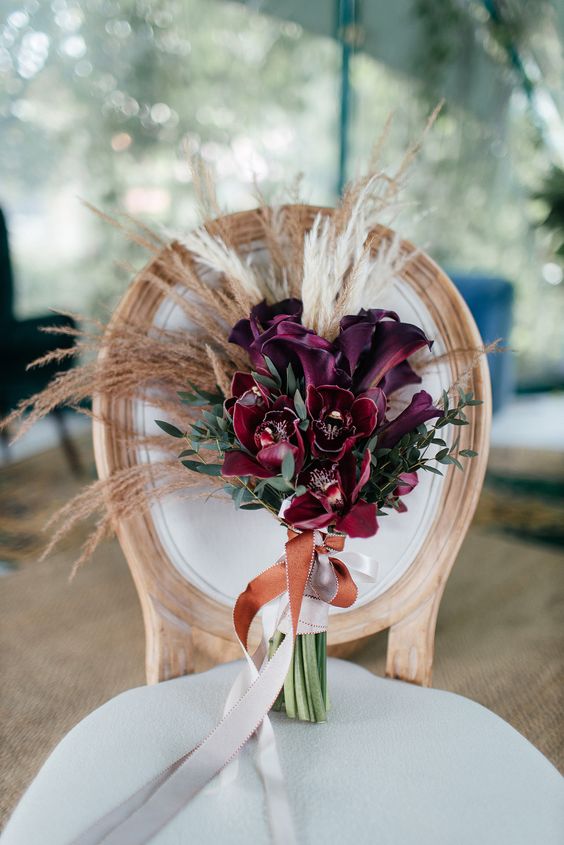 an elegant plum-colored calla wedding bouquet with greenery and pampas grass is a cool and eye-catchy solution