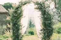 an ethereal Tuscany wedding arch covered with greenery and with white airy fabric is beautiful