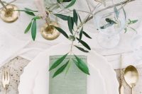 an ethereal wedding tablescape with greenery, blush candles in gold candleholders, green napkins and gold cutlery