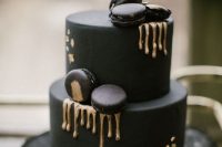 an ultra-modern black wedding cake with gold rip, black and gold macarons is a chic and cool idea for a modern moody wedding