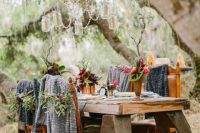 an uncovered wooden table and leather chairs, blankets and hanging jars, bold blooms and crystals for a relaxed fall woodland wedding