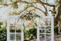 French double doors with greenery, white and pink blooms, matching blooms in planters are a great and chic wedding backdrop