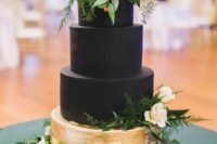 a black and gold wedding cake topped with greenery and blush blooms