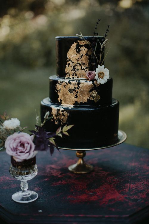 a black wedding cake decorated with gold leaf and a white bloom