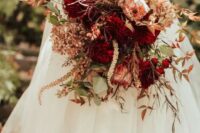 a bold fall wedding bouquet with deep red blooms, peachy ones, greenery and dark foliage is a cool idea