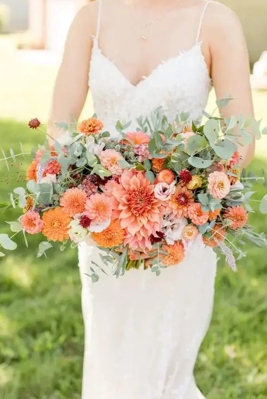 a bold summer wedding bouquet composed of orange and pink dahlias, pink ranunculus, smaller fillers and greenery