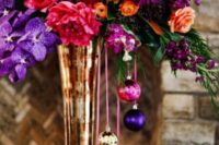 a bold winter wedding centerpiece in sumptuous colors and with bright ornaments hanging down from the vase