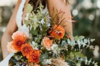 a bright and textural wedding bouquet with orange dahlias, some neutral and blue blooms, textural greenery, grass and twigs