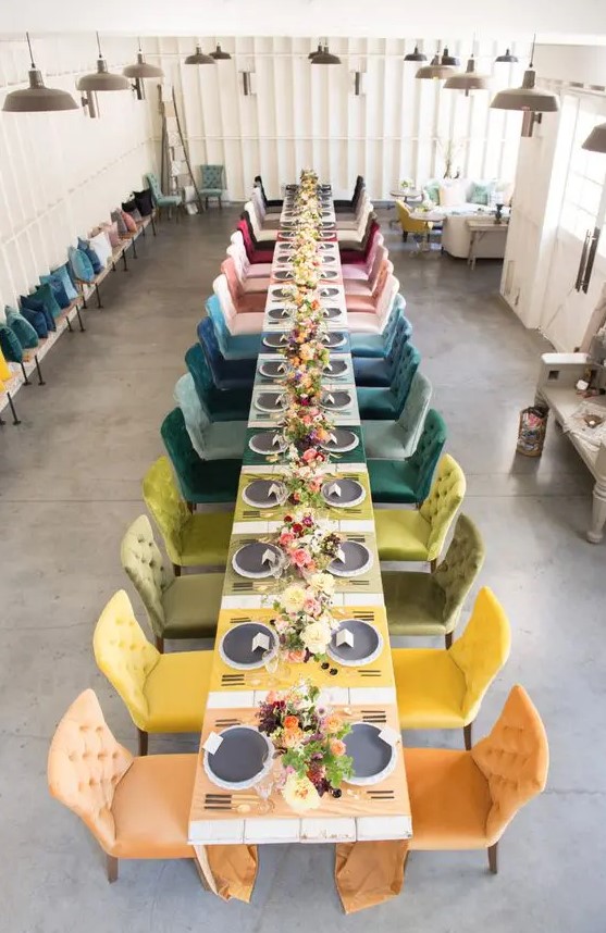 a bright rainbow wedding reception space with colorful placemats and matching velvet chairs is a very cool and bold solution