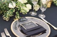 a chic black and gold wedding table setting with greenery and white blooms