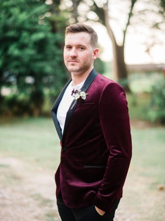 a chic groom's look with a burgundy velvet tux with black lapels and black pants calmed down with a white tee