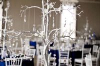 a chic wedding table with a navy tablecloth, a silver tree with crystals and white blooms plus candles