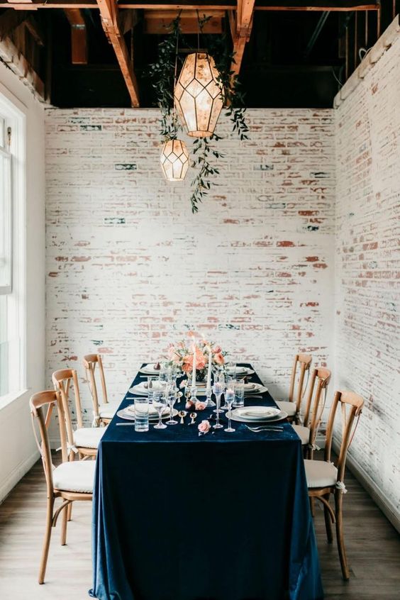 a chic wedding tablescape with a navy velvet tablecloth, coral blooms, candles and neutral porcelain and cutlery is amazing