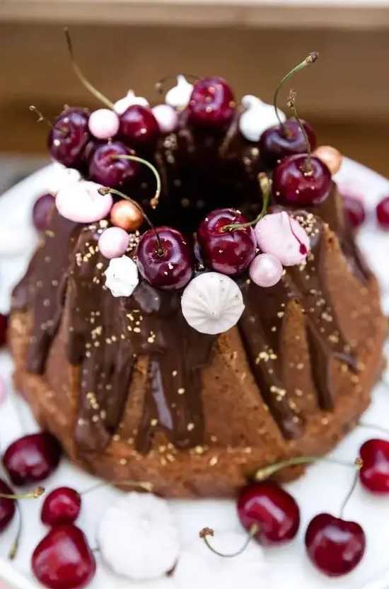 a chocolate bundt wedding cake with chocolate drip, gold leaf, fresh cherries, meringues and beads is a lovely and glam idea