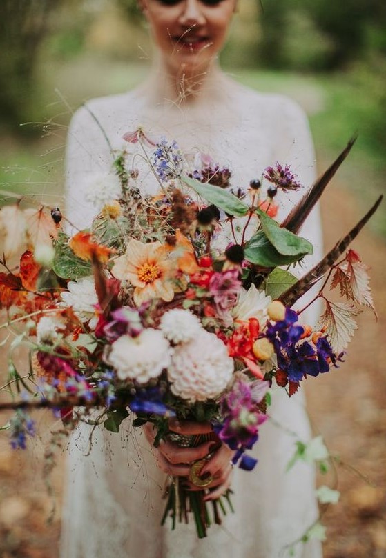 a colorful summer boho wedding bouquet in pink, orange, purple, blush, with lots of greenery and feathers