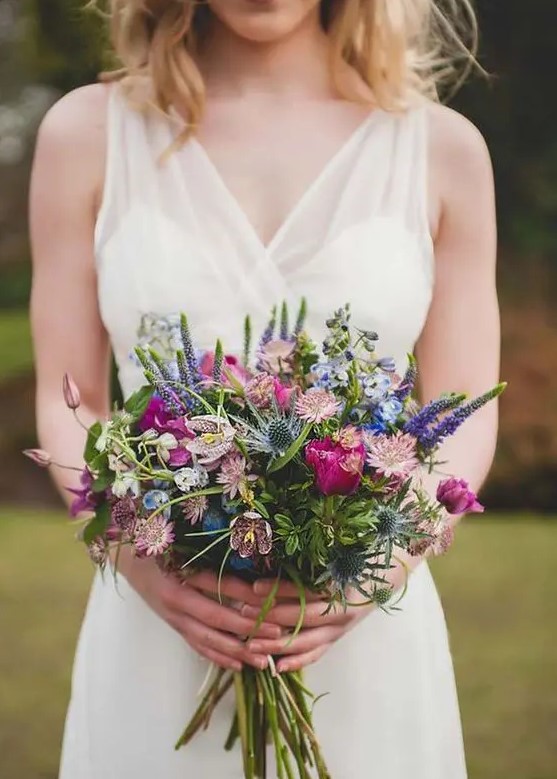 a colorful wildflower wedding bouquet with purple, blue and pink blooms and blue thistles