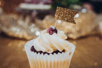 a cupcake topped with a raspberry and a gold gltiter flag topper is a lovely wedding dessert to enjoy