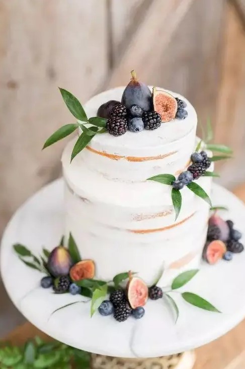 a delicate and pretty fall vineyard wedding cake - a semi-naked piece topped with fresh greenery, figs, blackberries and blueberries