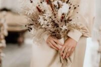 a delicate dried wedding bouquet of cotton, bunny tails, berries, twigs, dried foliage and grasses plus ribbons is ideal for fall