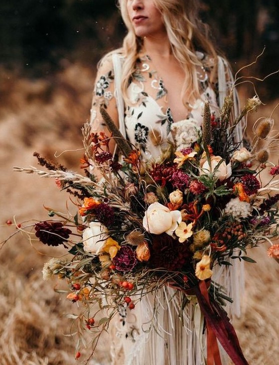 a fall wedding bouquet with marigold, burgundy and pink blooms, feathers, dried touches and berries