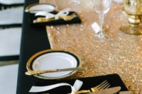 a glam black and gold wedding tablescape with a sequin runner, striped plates and a black velvet napkin