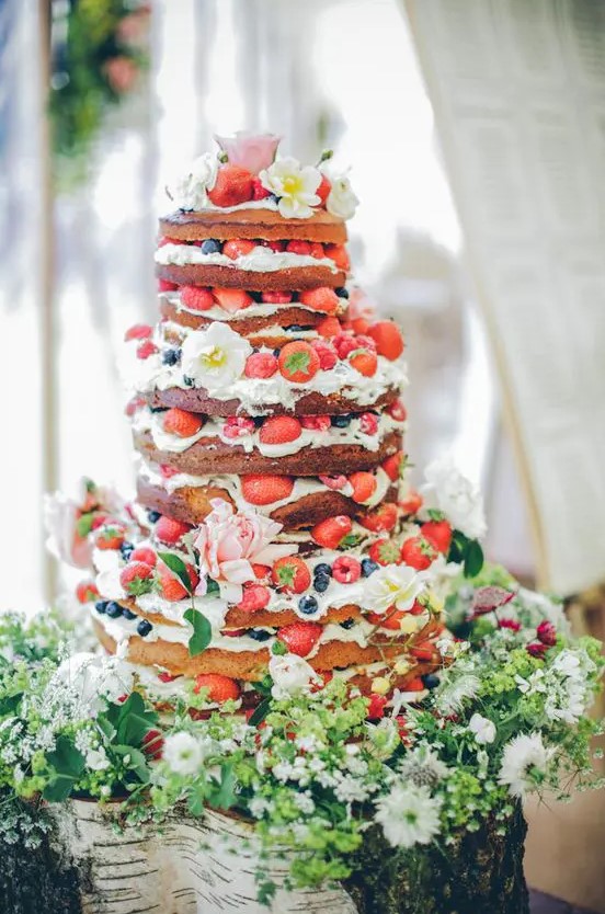 a gorgeous naked wedding cake with fresh bberries and white and pink blooms, with greenery is a lovely idea for a summer boho wedding