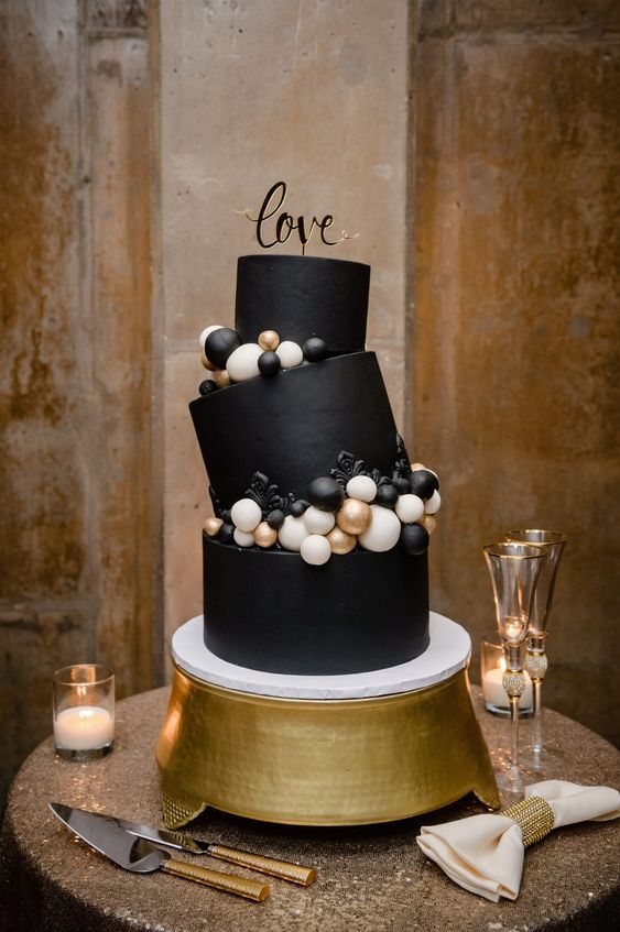 a gorgeous whimsy black wedding cake with black, white and gold ornaments and a gold calligraphy topper