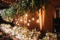 a greenery overhead wedding decoration with bulbs hanging down brings an outdoor feel to the space