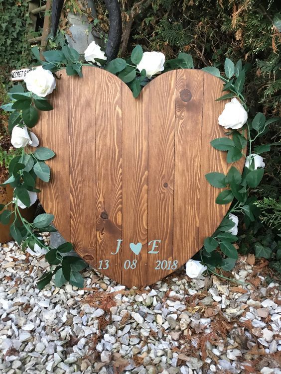 a heart-shaped plywood sign with the wedding date and monograms lined up with fresh greenery and white blooms