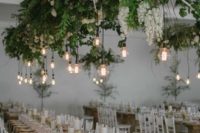 a lush greenery and white bloom installation with bulbs hanging down is a bold modern decor idea
