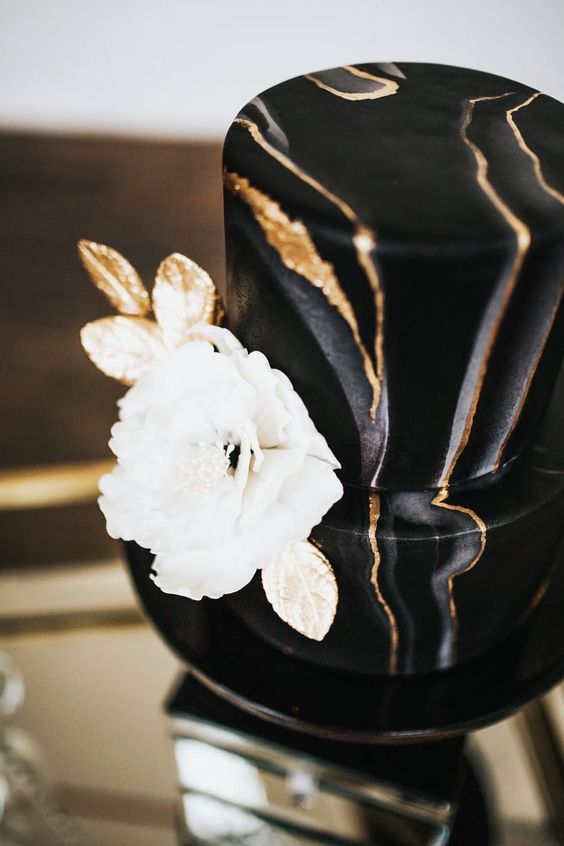 a marble black and gold wedding cake with a large white and gold sugar bloom