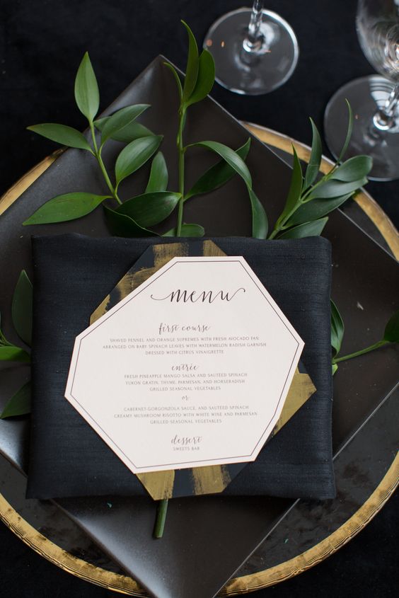 a modern place setting with a black charger with a gold edge and some greenery
