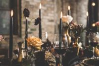 a moody wedding tablescape with black candles, black and gold chargers and a black runner and gold cutlery