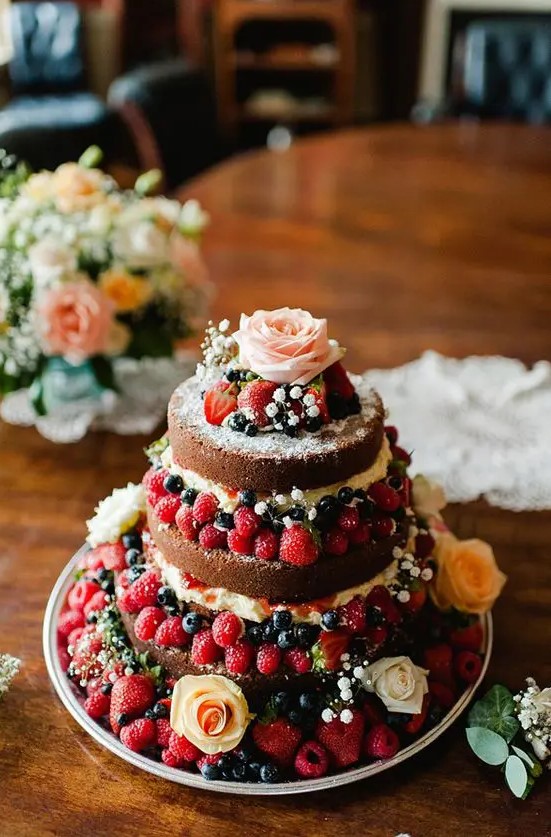 a naked wedding cake with lots of berries and fresh blooms, with greenery is a lovely solution for a spring or summer boho wedding cake