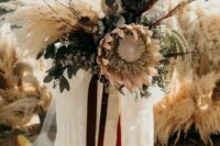 a neutral boho wedding bouquet of dried elements, feathers, berries, eucalyptus, king proteas and twigs