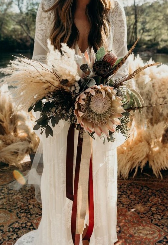 a neutral boho wedding bouquet of dried elements, feathers, berries, eucalyptus, king proteas and twigs
