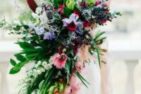 a romantic cascading and super textural wedding bouquet with pink, purple and red blooms plus much greenery