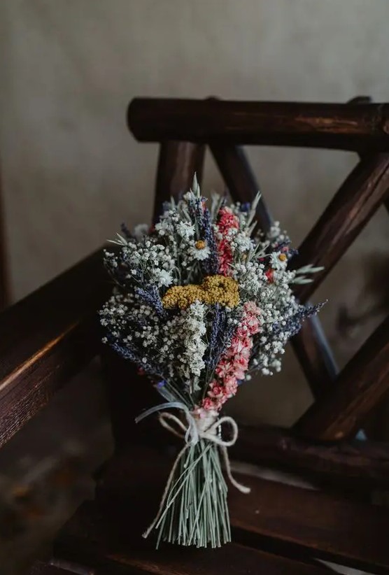 a small boho wedding bouquet of dried blooms in lilac, white, pink and yellow, with a yarn wrap is a chic idea for a boho bride