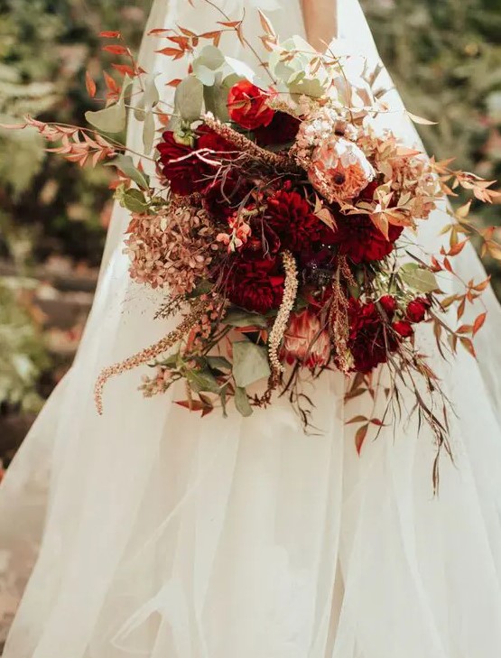a sophisticated wedding bouquet of deep red dahlias, pink king proteas, greenery and dried flowers is a lovely idea for a fall wedding