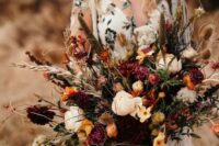 a super bold fall wedding bouquet of blush, yellow, orange and purple blooms, berries, greenery and soem grasses is a dimensional and textural idea